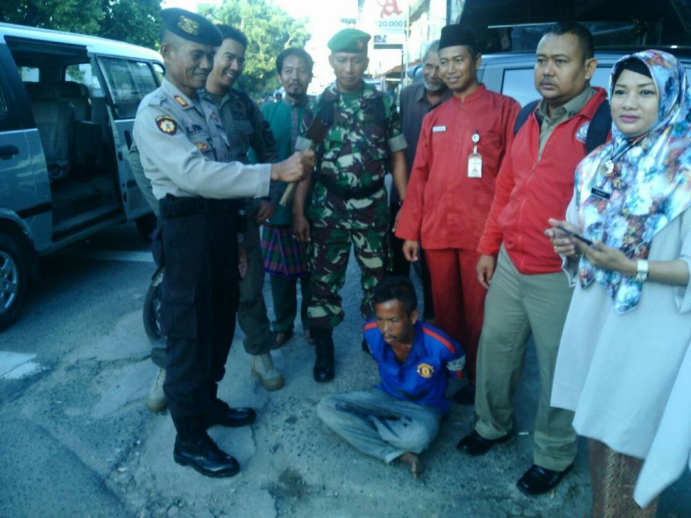 Seorang polisi (kiri) menunjukkan sebilah kapak yang diamankan dari tangan Usman (kaos biru)